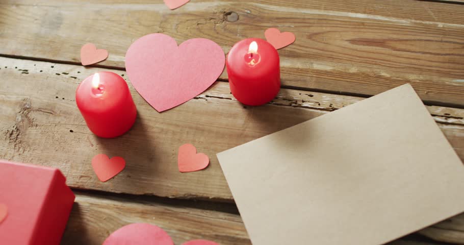 Paper hearts and gift with candles on wooden background at valentine