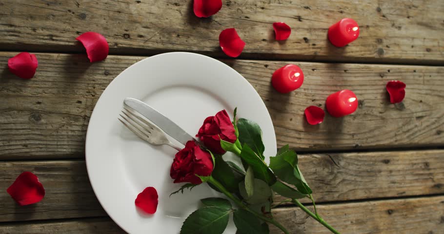 Candles and red roses on plate on wooden background at valentine