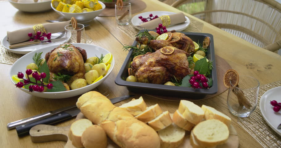 Camera starting close-up on roasted chickens and potatoes, panning holiday table showcasing feast. Gourmet, festive, rustic, celebratory, ensemble, elegance, homecooked