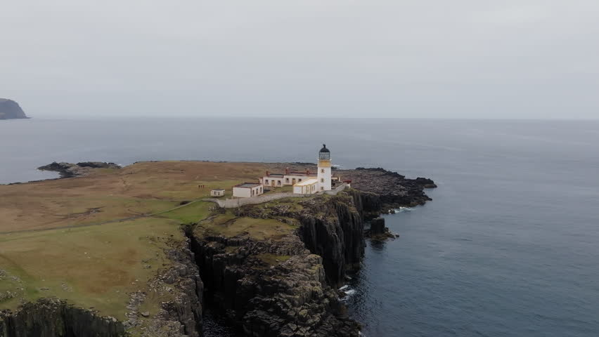 Neist Point Lighthouse standing on rugged cliffs above the Atlantic Ocean Scotland aerial orbit