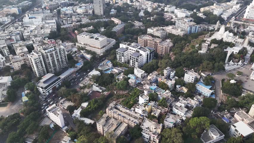 Cinematic aerial view of Hyderabad showcasing dense residential blocks, tree-lined streets, and mid-rise buildings surrounding the hilltop Birla Mandir, blending greenery with structured urban develop