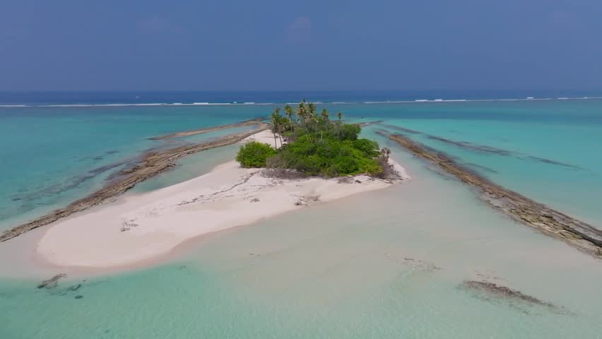 Aerial drone flight over a rocky tropical islet in the Maldives surrounded by turquoise lagoon and clear ocean with natural rugged island scenery