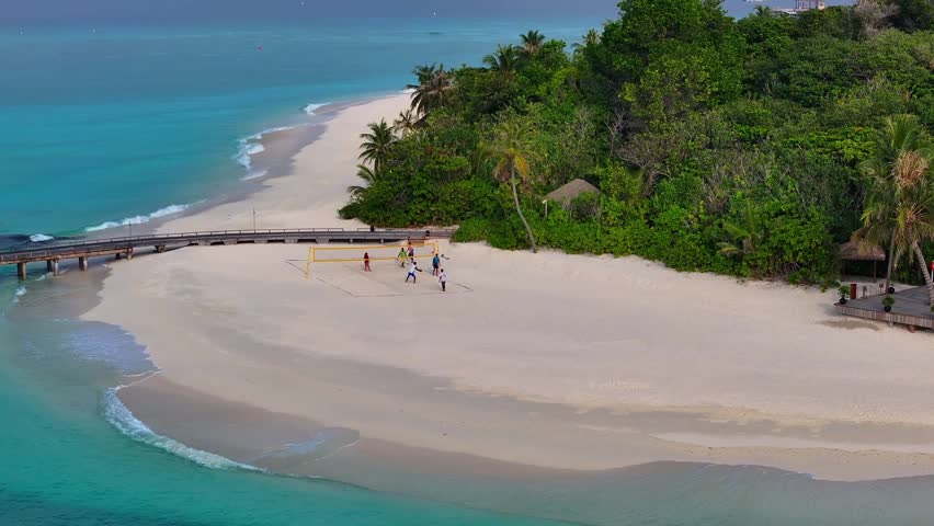 Aerial view of children playing beach volleyball on a tropical resort island in the Maldives with white sand, turquoise water and sunny seaside atmosphere.