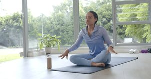 Seated upright African American woman leaning, speaking and showing chest breath on mat with bottle. Yoga, breathwork, posture, mobility, instructor, dumbbells, sunlight - Powered by Shutterstock - Get 15% off with code: PIKWIZARD15
