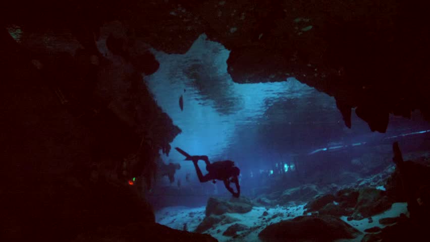 Scuba diver swims toward bright natural light illuminating cave exit in Cenote Dos Ojos, Quintana Roo, Mexico