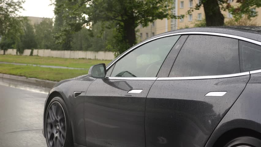 Modern electrical automobile driving at urban road on rainy day. Ecology friendly car riding moving along motorway. Electric vehicle riding through empty highway. Concept of green innovation. Slow mo