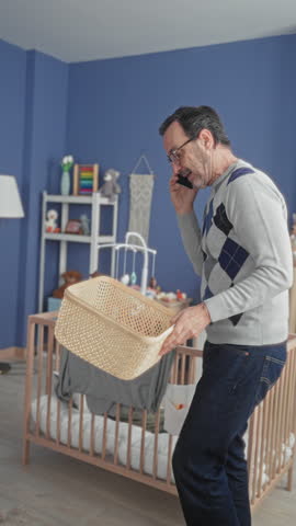 Man on phone placing stuffed rabbit into basket beside crib in baby room building; care organization.