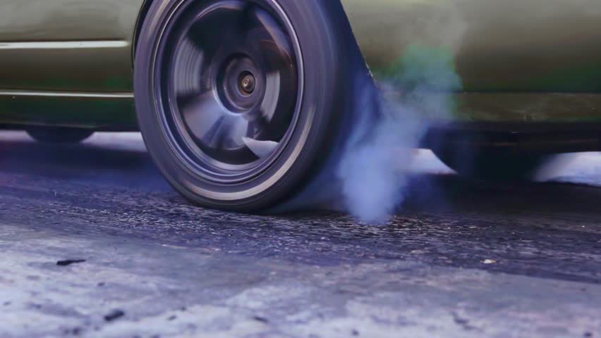 Close up dynamic shot of car wheel burning rubber creating smoke clouds. Fast motion, powerful engine, street racing action.