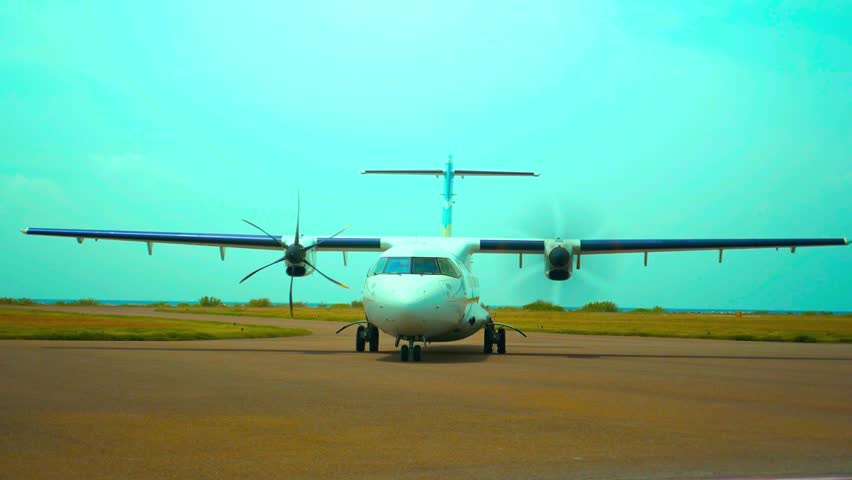 Front view of small commuter plane on runway against bright blue sky, with propellers spinning. This dynamic footage showcases aviation and travel in a vibrant, outdoor setting.