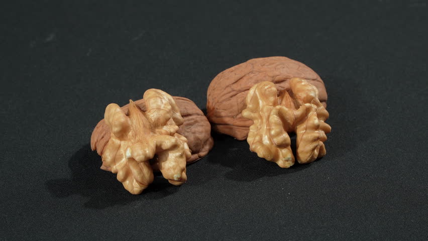 Macro of two shelled walnut kernels resting on empty shells against a black background. Premium organic anatomy and brain food concept.