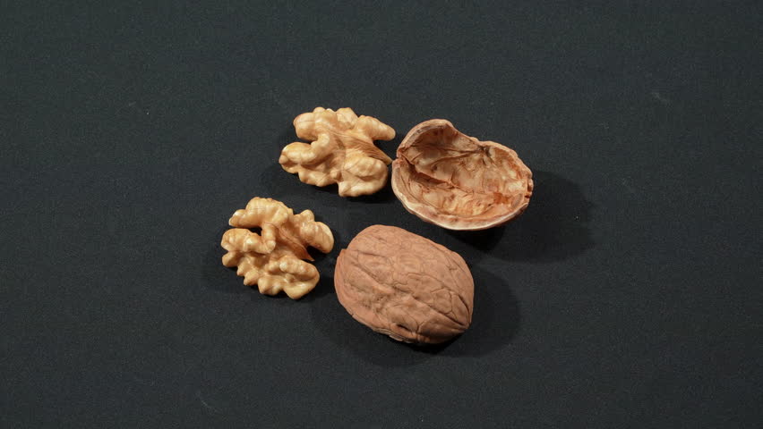High angle macro of two shelled walnut kernels next to two empty cracked shells, dynamic rotating on a black background. Premium healthy brain food concept.
