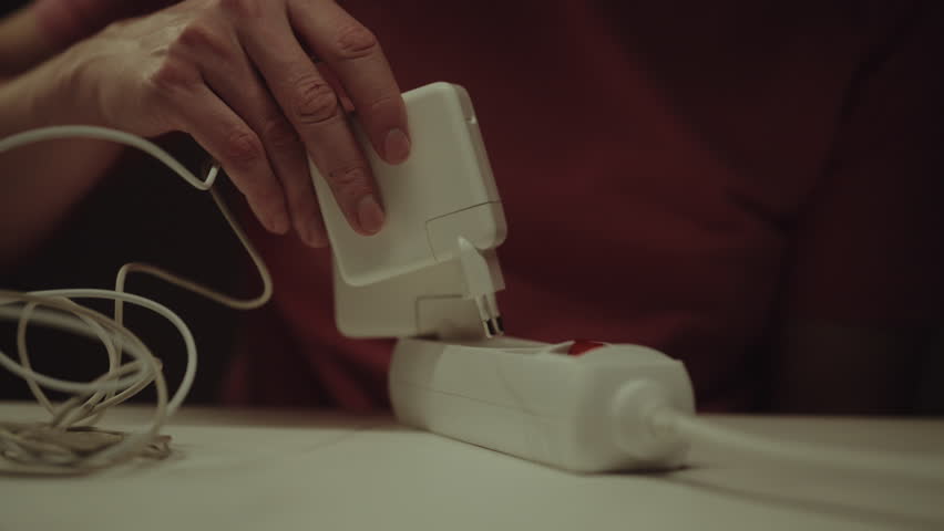 Male hands connecting white power adapter to extension cord on white table, providing electricity to charge laptop computer battery and ensuring continuous workflow, close-up. Shooting in slow motion.