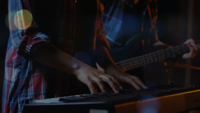 Playing drummer in plaid shirt striking snare, toms and cymbals in studio with keyboard, bass neck. Stage, ensemble, rehearsal, lighting, ambience, bokeh, groove