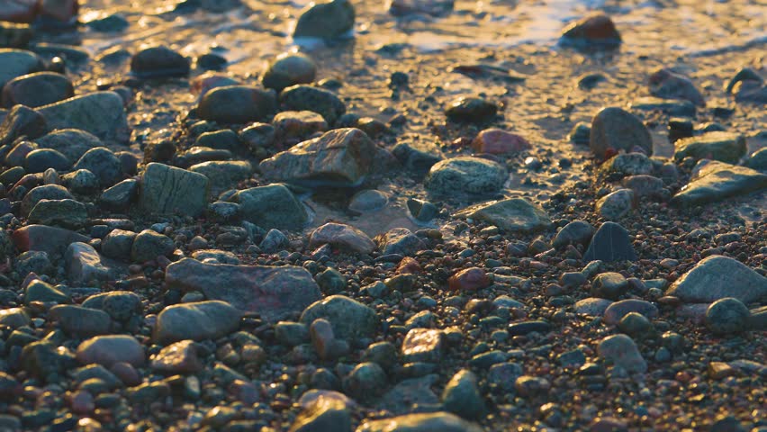 Waves crashing over colorful pebbles on beach shoreline during golden hour natural texture scene