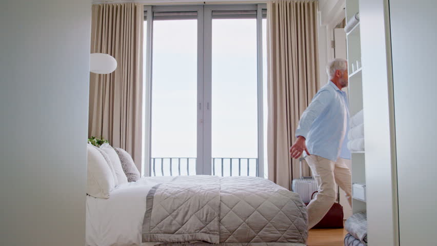 Travel, man and jump on bed at hotel for relax, vacation and tired with comfort on mattress. Mature person, holiday and resting in bedroom of motel for break, peace and calm with hospitality on trip