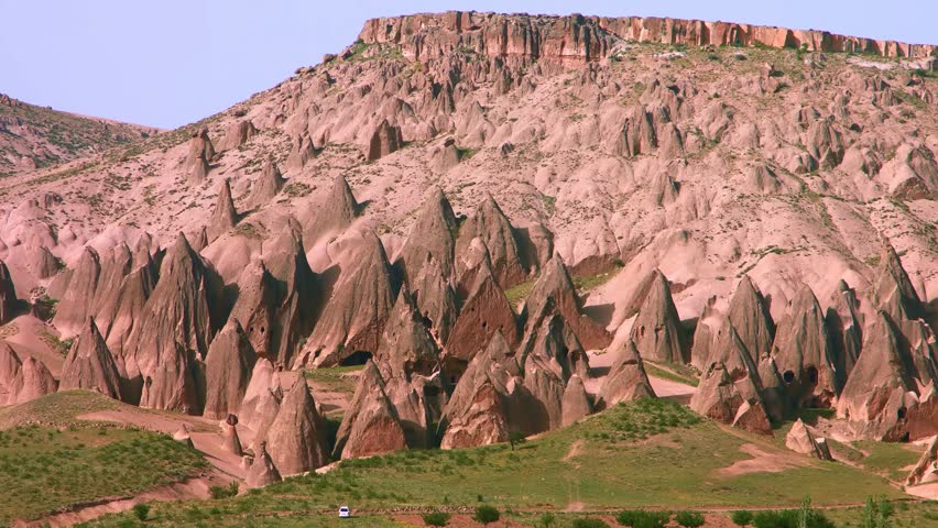 A scenic wide shot showcasing the arid, desert landscape of the Red Valley in the Cappadocia region of Turkey. The image captures the distinctive, conical "fairy chimneys" and unique geological sandst