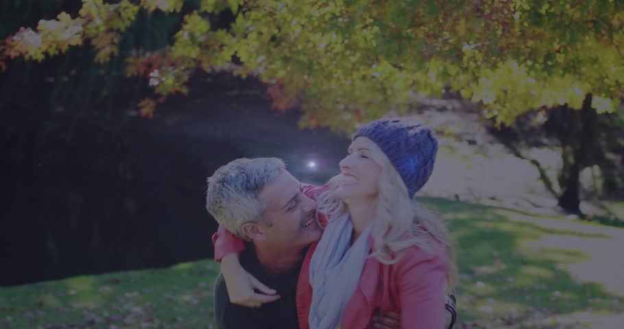 Man lifting woman while laughing in park, expressing love with animated lens flare for lifestyle ad. Couple, embrace, autumn, foliage, leaves, sunlight, backlit