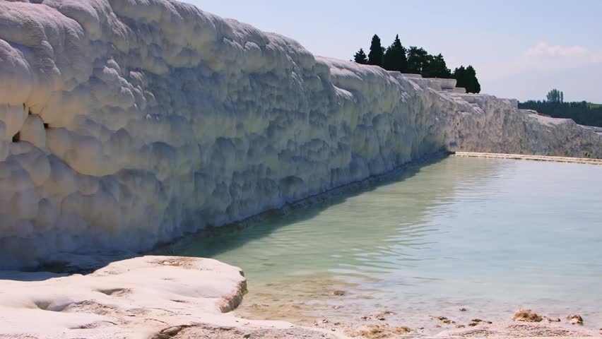 Footage capturing the stunning natural wonder of Pamukkale, Turkey. The scene features the iconic, brilliant white travertine terraces, formed over millennia by calcium carbonate deposits from mineral