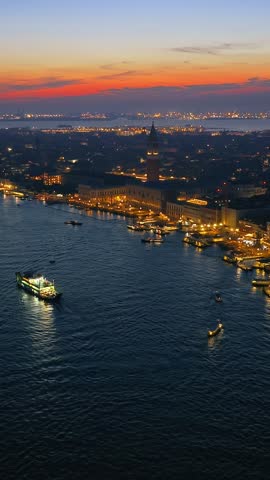 Drone footage captures illuminated Venice waterfront and historic buildings at dusk with calm sea and colorful sky.