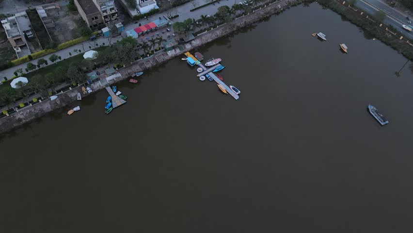 Boats docked at a pier on a lake with industrial background and hazy sky.