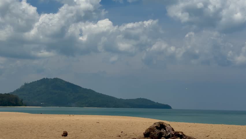 Scenic tropical beach with turquoise sea and a green mountain under a cloudy blue sky. Beautiful coastal landscape in Phuket, Thailand, perfect for travel, vacation and nature concepts.