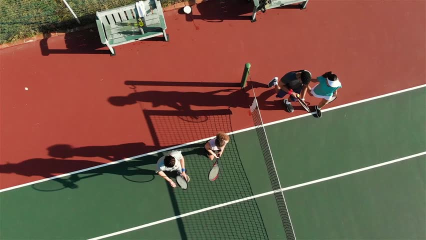 Diverse tennis teammates stepping to net as match ends tapping rackets shaking hands exiting court. Tennis, sportsmanship, teamwork, outdoor, active, competition, recreation