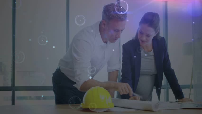 Man pointing at laptop activating animated HUD while woman marking plans to finalize project. Blueprints, collaboration, teamwork, planning, architecture, meeting, office