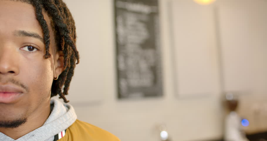 African American man in his twenties noticing off camera prompt, smiling by chalkboard menu in cafe. Portrait, expression, casual, warm, candid, interior, approachable