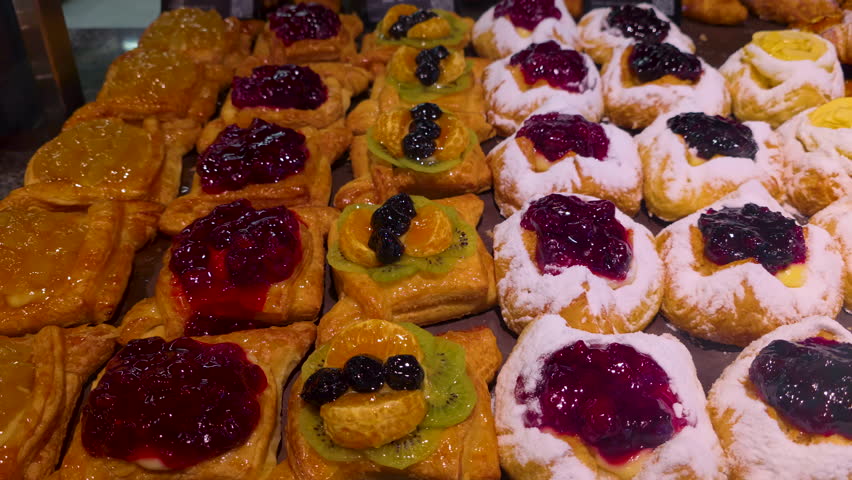 Assorted sweet pastries with fruit topping on bakery display, freshly baked dessert selection with jam glaze and powdered sugar arranged in rows