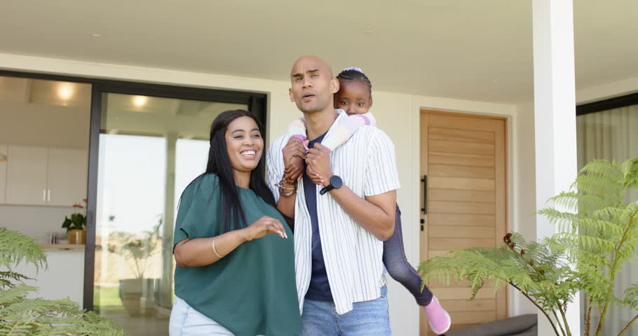 Spotting visitor, diverse family standing on porch steadying daughter while smiling and waving. Family, porch, happiness, togetherness, outdoor, lifestyle, modern
