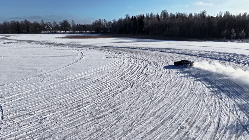 Racing Car Drifts Across A Frozen Snowy Field, Leaving Tire Tracks And A Snow Trail. - aerial follow shot