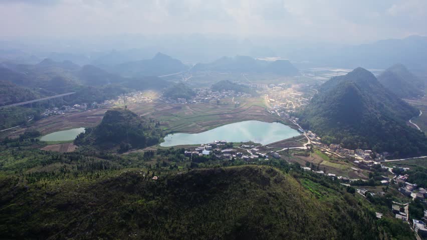 Aerial panning view of karst mountains and rural village with terraced fields in Guilin, Guangxi, China, dramatic clouds casting shadows over landscape