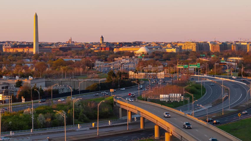 Washiongton DC. Aerial view of Washington DC during sunset with the Washington Monument and city skyline in the background. The sky is a gradient of pink and orange hues.