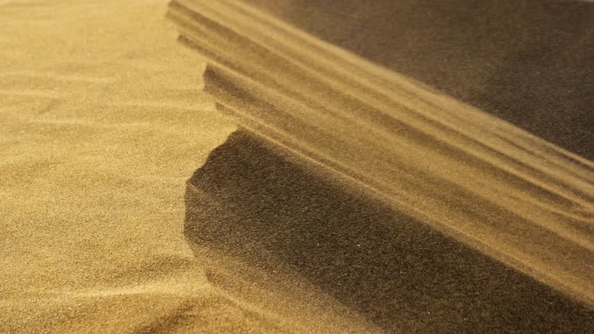 Strong wind sweeps a sand storm over the edge of a desert dune. Moving sand particles create dynamic surface patterns. Extreme close up detail shot