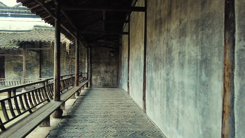Hangzhou, China. A photograph of a traditional courtyard with wooden benches and a tiled roof. The architecture is characterized by its rustic charm.