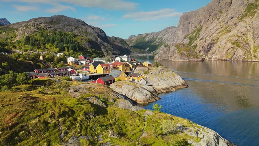 Traditional red and yellow cabins stand in the Nusfjord fishing village of the Lofoten Islands, Norway. Drone aerial reveals steep mountains surrounding the fjord of Nusfjord, Norway