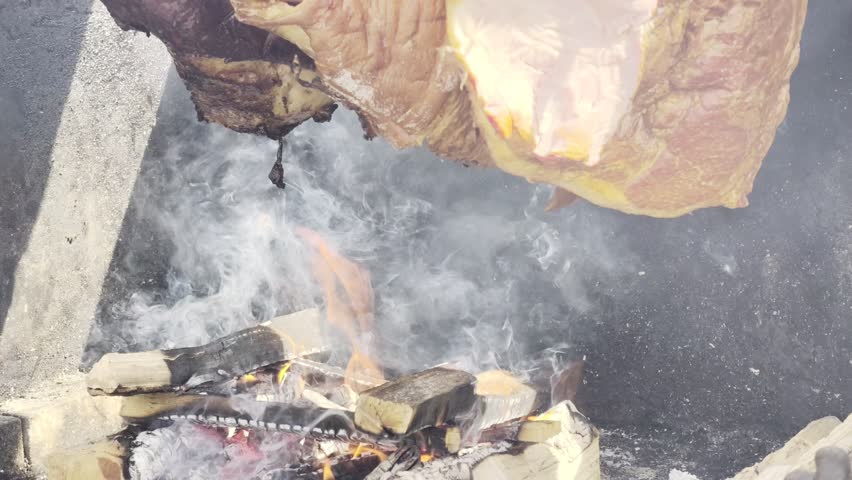 Roasting meat on open fire with flames and smoke, large cuts on metal spit, HDR Dolby Vision 4K rustic barbecue cooking close up