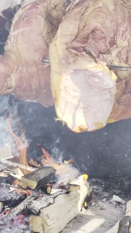 Roasting meat on open fire with flames and smoke, large cuts on metal spit, HDR Dolby Vision 4K vertical video rustic barbecue cooking close up