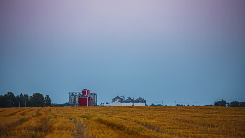 Golden wheat field with red barn under cloudy sky at sunset
