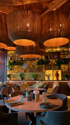 Modern restaurant interior with woven lamps and plant shelves. View of a dining room featuring oversized woven pendant lights and a decorative shelf with green plants.