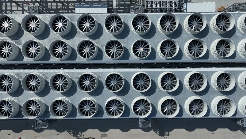 Aerial tilt from cooling fans to mechanical systems and data center buildings, revealing industrial infrastructure, piping, and HVAC supporting AI and cloud computing operations.