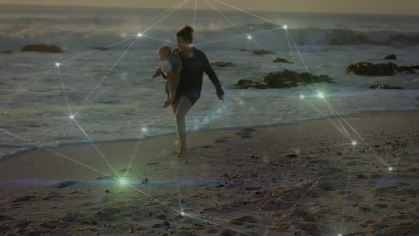 Upon seeing waves, woman carrying infant walking to surf, pausing, reaching so child can touch sea. Beach, shoreline, sunset, calm, balance, barefoot, parent