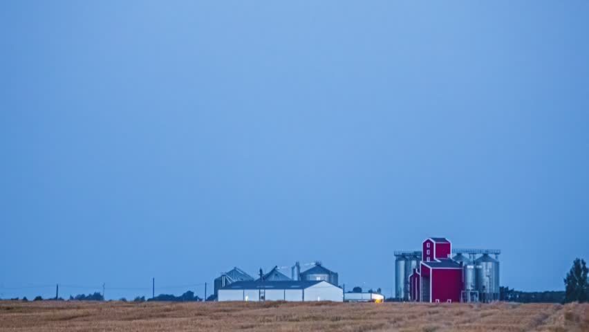 Farm field and red silo stand under blue dusk sky with open rural horizon in timelapse
