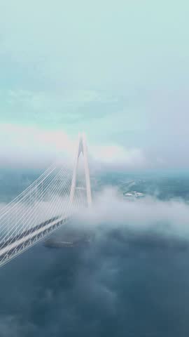 This high quality 4K vertical aerial video captures a breathtaking and cinematic perspective of the Yavuz Sultan Selim Bridge in Istanbul, Turkey. The footage features a steady drone glide above a sea of thick, white clouds and ethereal morning mist, showing the bridge’s massive 322 meters high pylon and intricate cables stayed design emerging into the clear blue sky. As the camera pans, the bridge deck is visible cutting through the fog, with the deep blue waters of the Bosphorus and the lush green landscape of the northern coastline occasionally peeking through the clouds.

The vertical (9:16) orientation is perfectly optimized for mobile first platforms such as shorts. The contrast between the monumental engineering marvel and the soft, dreamlike atmosphere of the fog creates a powerful and sophisticated visual narrative. This clip is an ideal asset for travel documentaries, architectural portfolios, and editorial content focusing on global infrastructure or Turkish landmarks. It beautifully documents the bridge as a symbolic link between the continents of Europe and Asia, offering a serene and majestic depiction of modern transit at the gateway to the Black Sea.