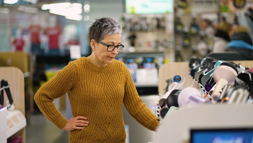 Mature woman choosing new hairdryer in electronics store