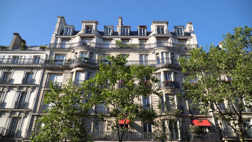 Golden afternoon sunlight illuminating a historic building facade and lush green trees on Boulevard Saint Germain in Paris, France.