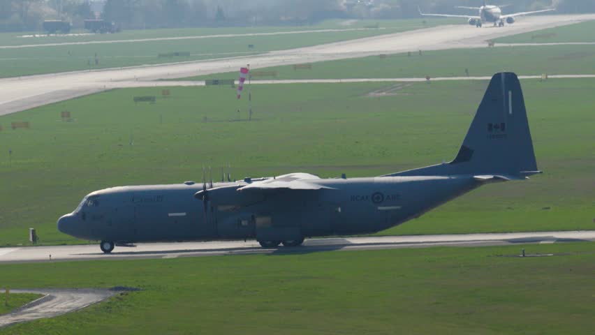 A magnificent Lockheed C-130 Hercules roars to life as it takes off from the airfield. The sun shines brightly, casting shadows over the green landscape below, creating a remarkable view.