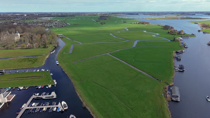 Panoramic aerial view of lush green Dutch polders and meadows crisscrossed by canals. A classic Netherlands landscape featuring a traditional windmill, waterways, and rural countryside scenery.
