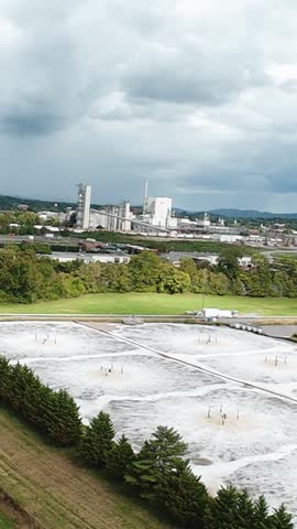 Vertical screen Aerial View Industrial Wastewater Ponds Kingsport Tennessee Under Stormy Sky, Treatment Plant Silos And Processing Basins Across Green Field, Tree Line And Access Road