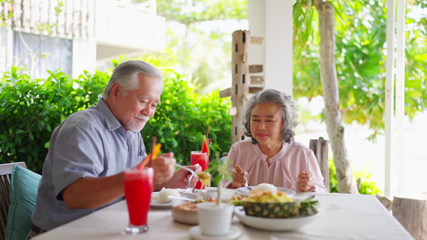 Happy Asian senior couple enjoying meal together at restaurant, elderly people with healthy eating lifestyle, cheerful family dining and bonding during retirement life, positive aging and relationship.